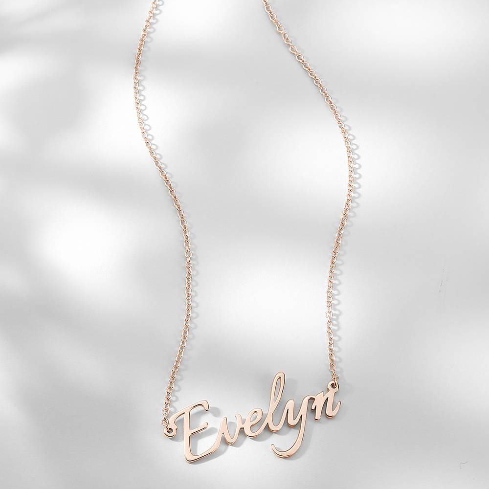 Rose-gold-tone script name necklace displayed on white fabric