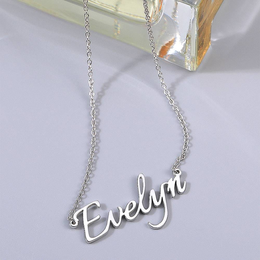 Silver-tone script name necklace displayed beside a glass bottle