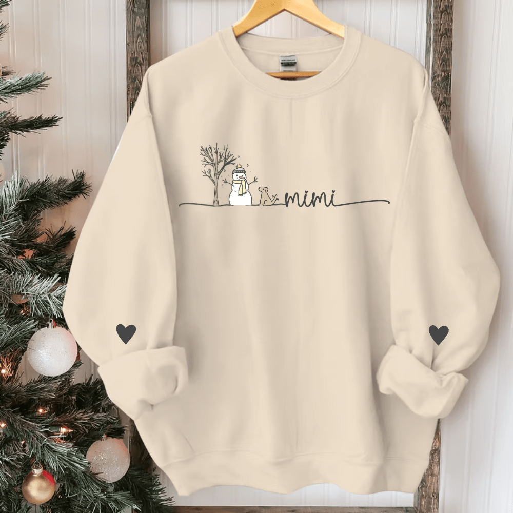 Beige Mimi sweatshirt on a hanger with a snowman and tree design and heart details on both sleeves